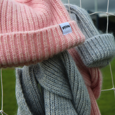Pink beanie and gray scarf with a visible brand label against a blurred background