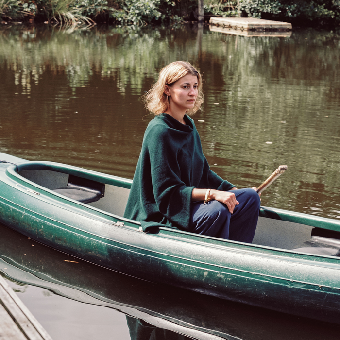 Woman in a green poncho sitting in a canoe on a calm lake