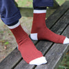 Red socks with white accents worn by a person sitting on a wooden bench.