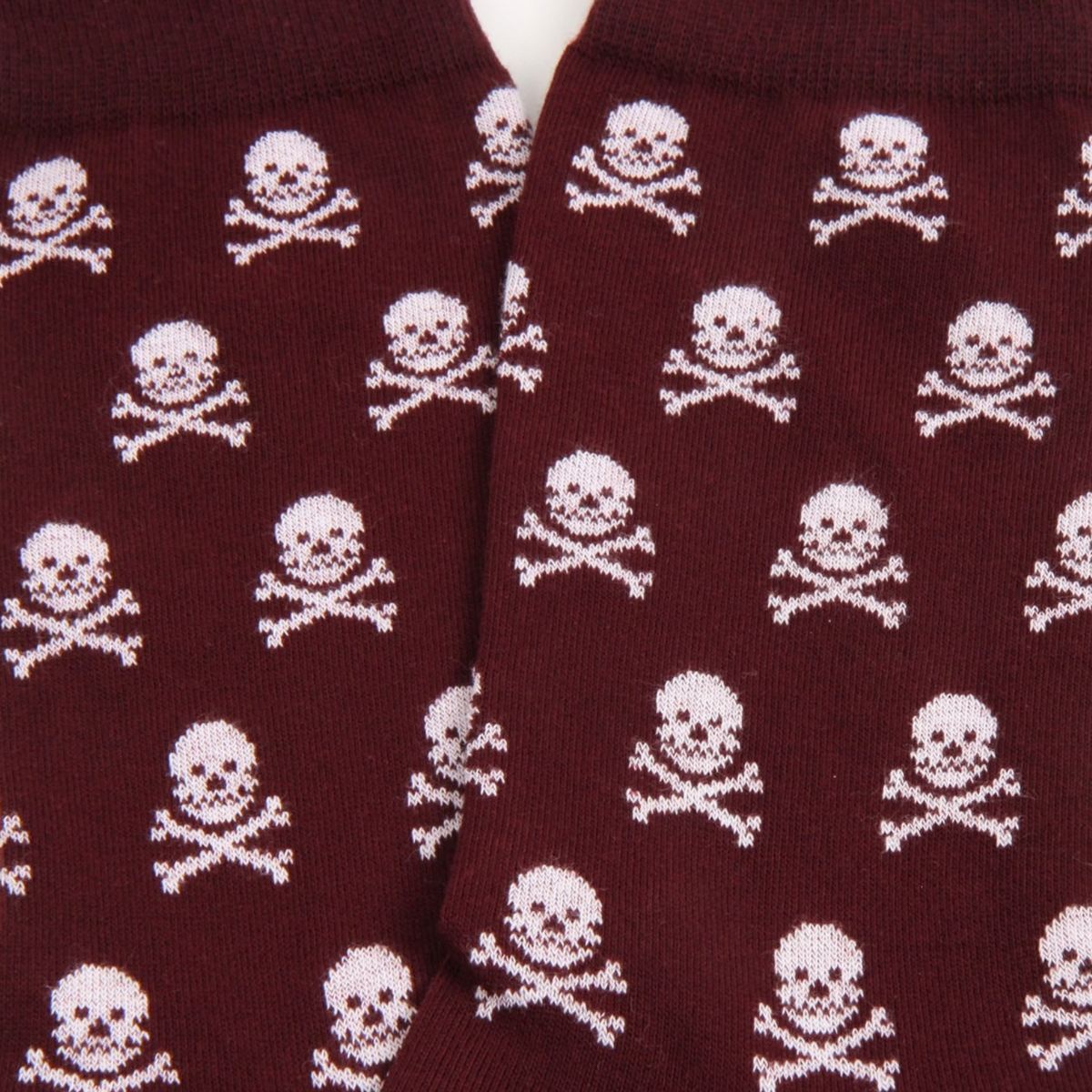 A close-up of a pair of dark burgundy socks with a repeating white skull and crossbones pattern.