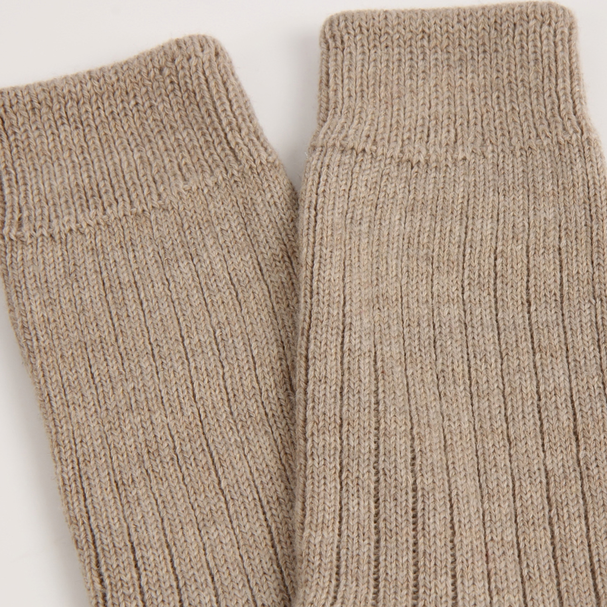 A pair of ribbed knit crew socks in a light beige/tan color, featuring a dark navy logo and text on the sole, displayed against a solid white background.