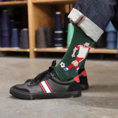 Person wearing green socks with a soccer player design, black shoes with red and white stripes, in a workshop setting.