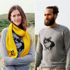 A collage of two images, one showing a woman wearing a gray wool sweater with a corgi motif in intarsia knit, and the other showing a man wearing a similar sweater. Both are modeling the sweaters outdoors.