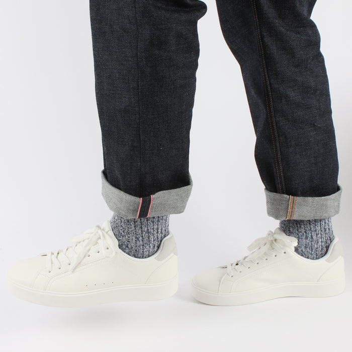 Person wearing dark jeans with rolled-up cuffs, white sneakers, and navy marl  socks on a white background