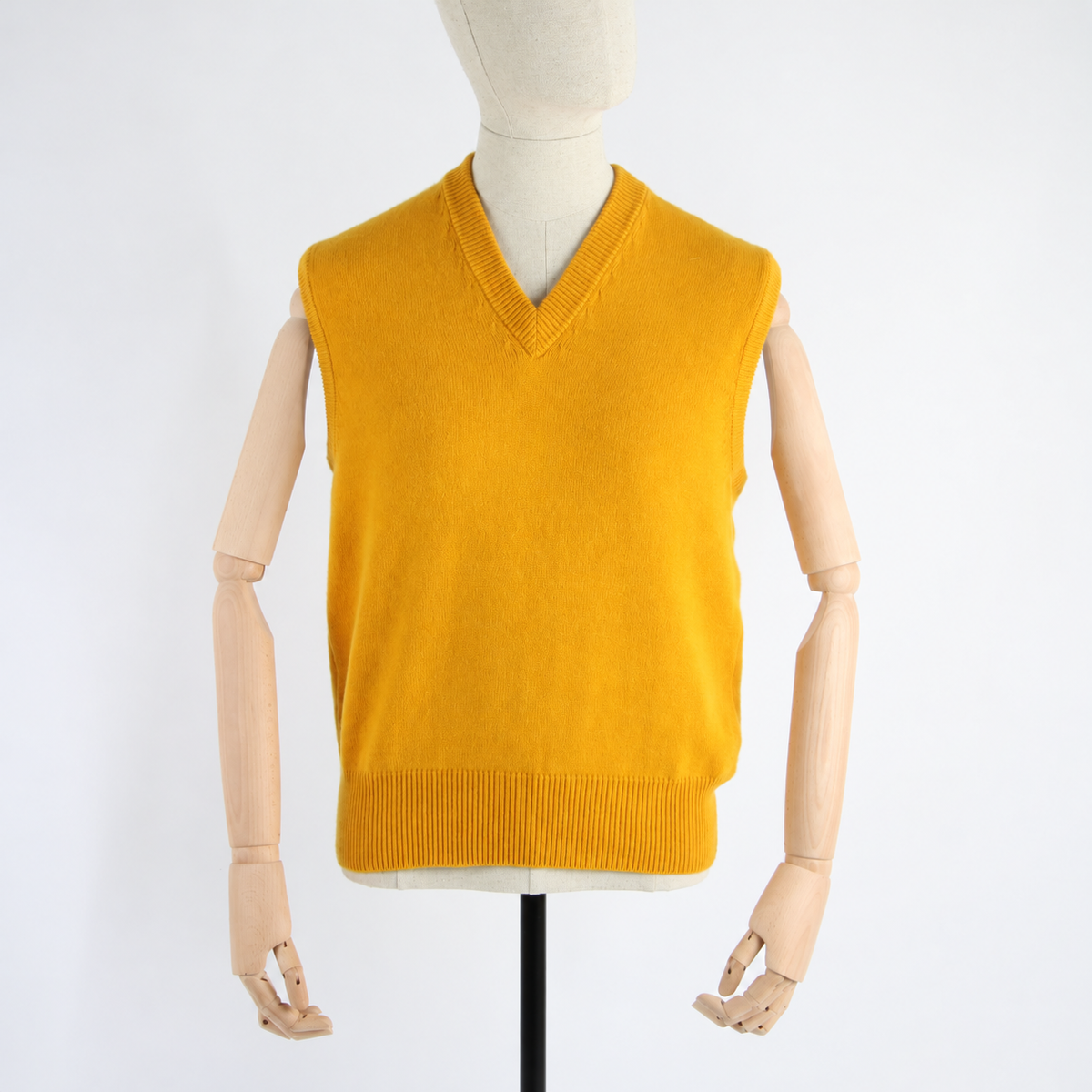 A mustard yellow knit sweater vest displayed on a wooden mannequin torso against a plain white background.