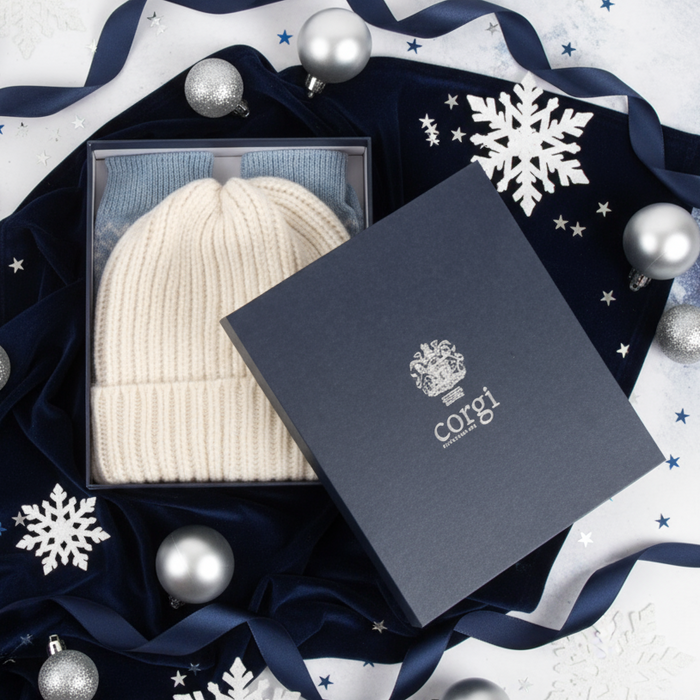 White knit beanie and blue fair isle socks inside a branded navy box on a white background