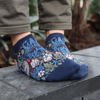 A pair of blue trainer socks with a floral pattern, featuring the 'Strawberry Thief' design by William Morris, worn on someone's feet.
