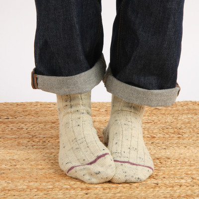 Person wearing beige socks with dark jeans on a woven surface