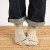 Person wearing beige socks with dark jeans on a woven surface