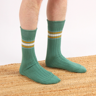 Green socks with white and yellow stripes worn by a person on a textured surface.