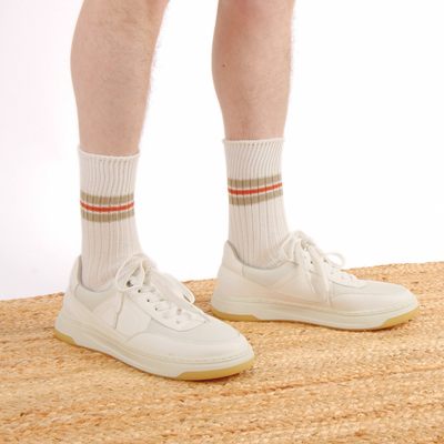 White sneakers and socks with striped cuffs on a neutral background