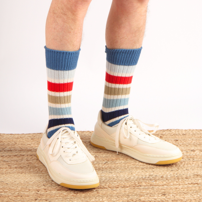 Colourful striped socks with blue, red, and beige pattern worn with white sneakers on a neutral background