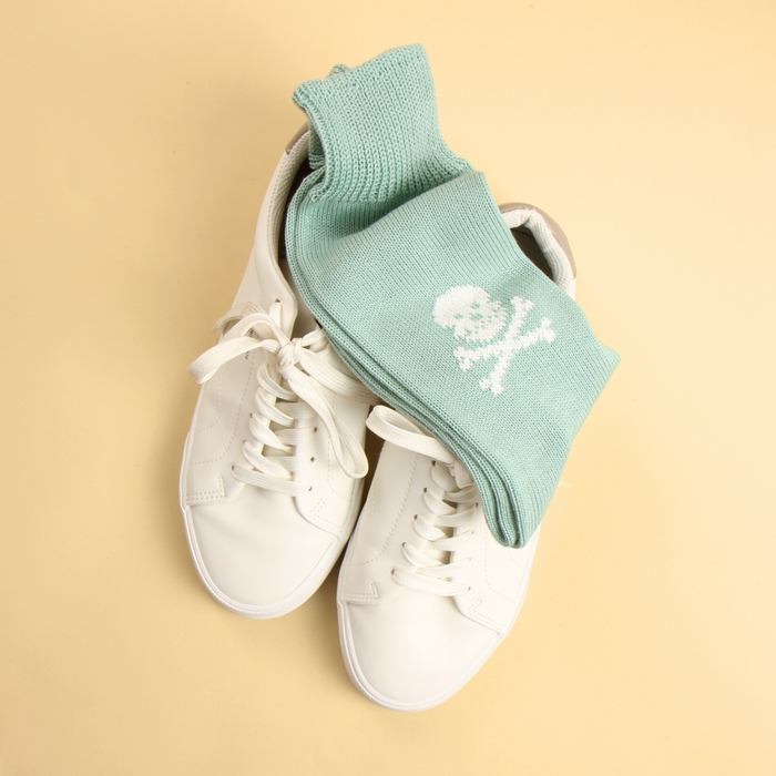 White sneakers with light aqua socks featuring a skull design on a beige background