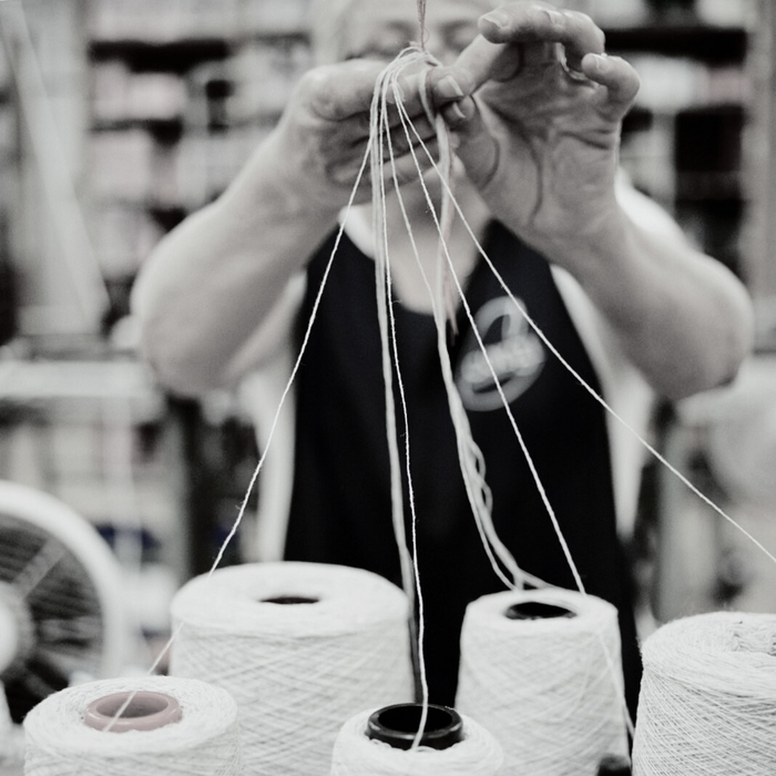 a person standing at a knitting machine with spools of yarn