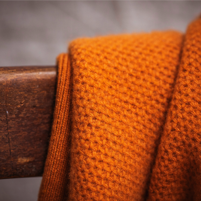 Close-up of an orange knitted fabric draped over a wooden surface with a blurred background.