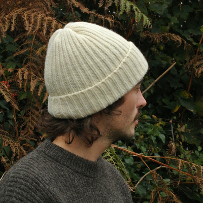 Person wearing a ecru knit beanie and sweater in front of green foliage
