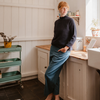 Person standing in a kitchen with white cabinets and a wooden countertop wearing a navy British wool roll edge sweater