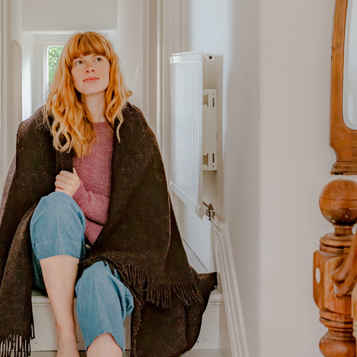 Woman sitting on a staircase wrapped in a brown blanket, wearing a pink sweater and blue jeans.