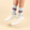 White sneakers with light blue socks featuring red and blue stripes on a yellow background