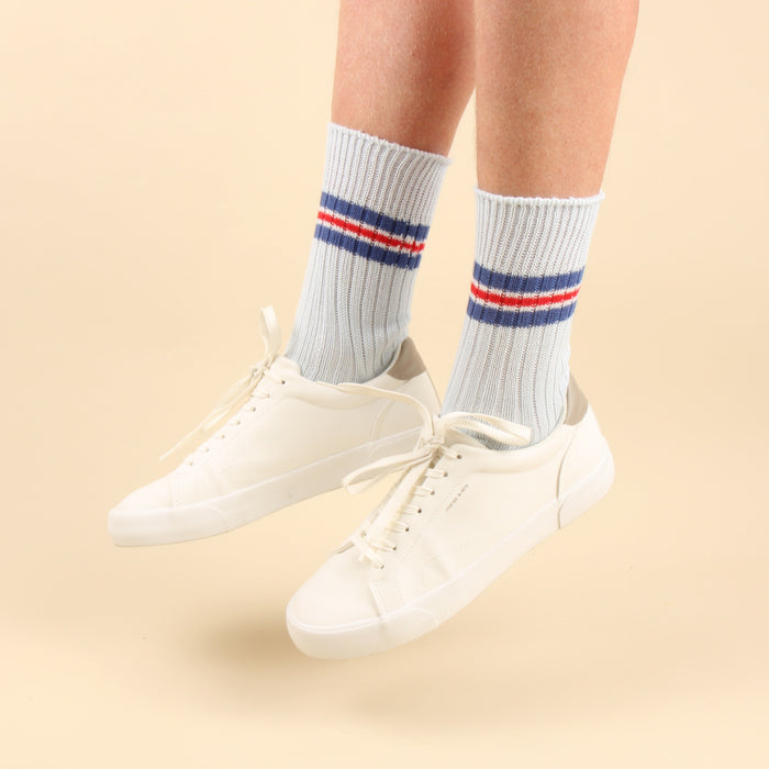 White sneakers with light blue socks featuring red and blue stripes on a yellow background
