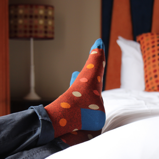 Colorful polka dot socks in a rich rusty red being worn on a bed with a blurred background