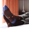 Person wearing brown socks with red and blue polka dots on a bed.