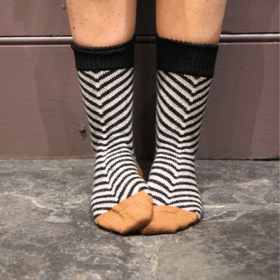 Person wearing black and white striped socks with gold toes on a stone floor.
