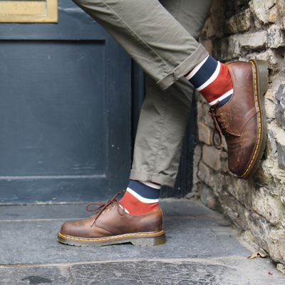 Person wearing brown leather shoes and colorful socks against a stone wall.