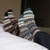 2 Pairs of feet wearing patterned socks on a comfy bed.