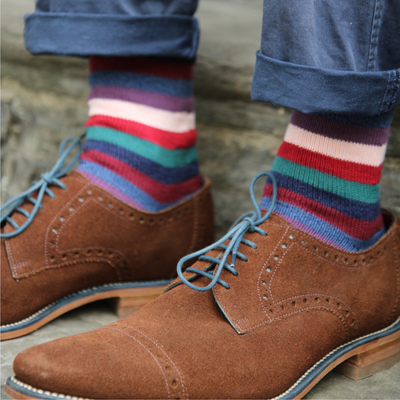 Brown dress shoes with striped socks on a stone surface