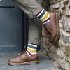 Person wearing brown shoes and colorful striped socks against a stone wall.