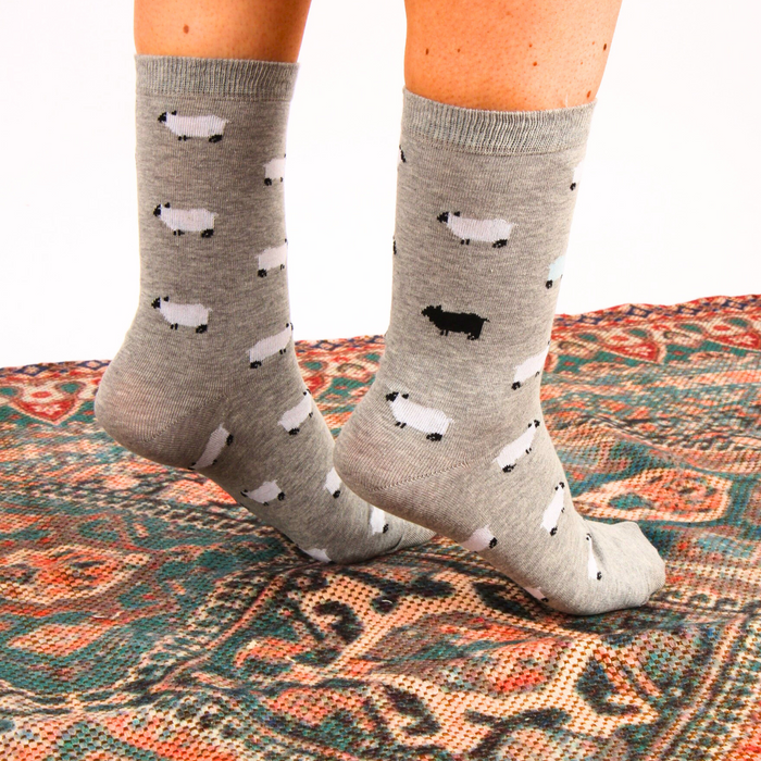 Gray socks with black and white sheep pattern worn on a patterned rug