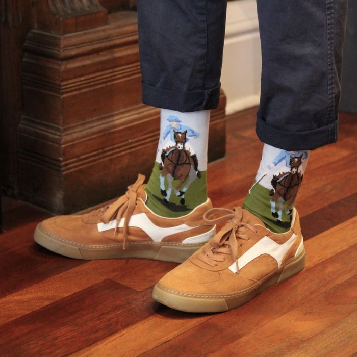 Person wearing tan sneakers and navy pants with socks featuring horse illustrations on a wooden floor.
