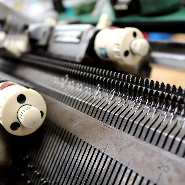 Close-up of a knitting machine with visible yarn threads and needles, illustrating the handcrafted process of making knitwear.