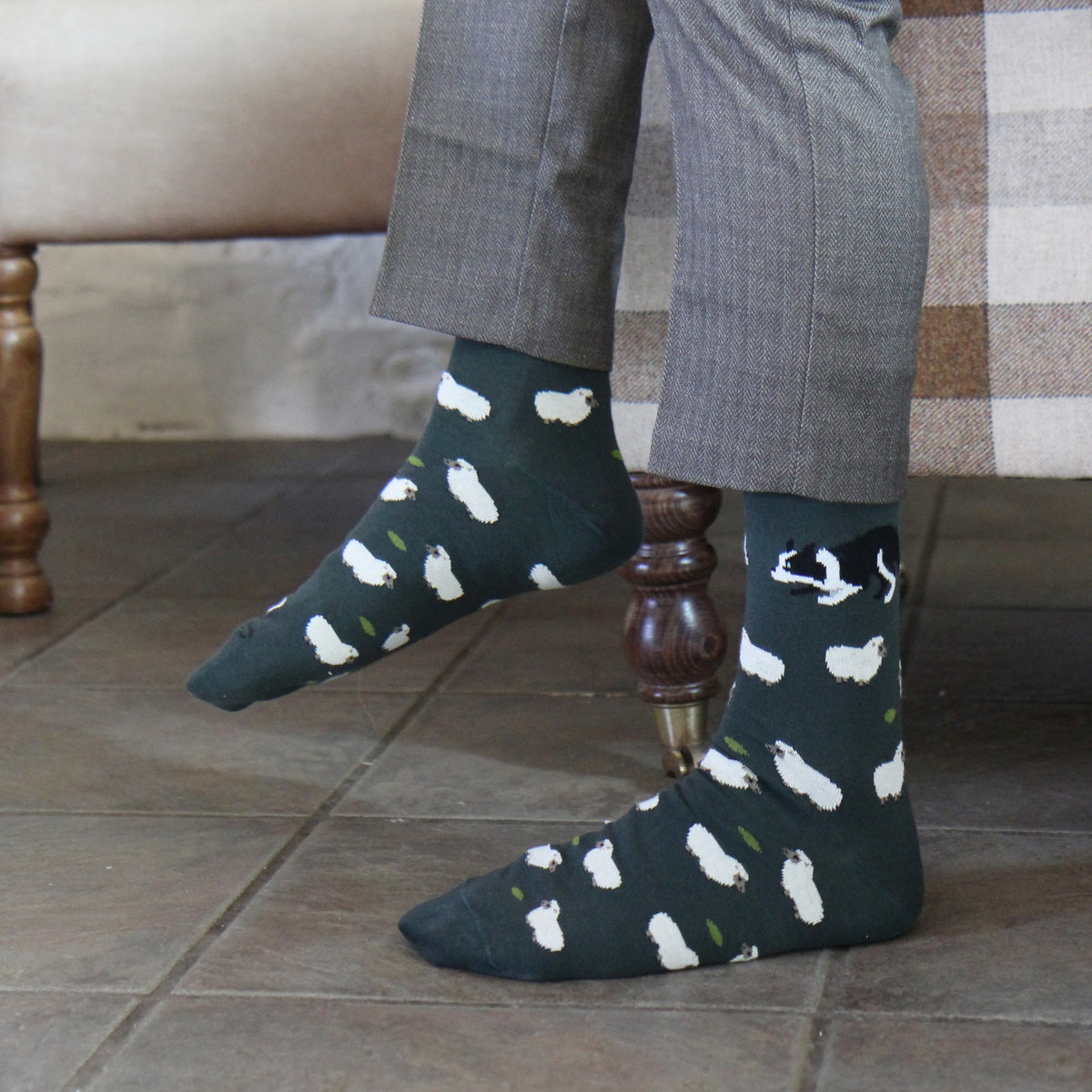 A person wearing dark green crew socks with a white and black dog print, paired with gray trousers, sitting on a bench.