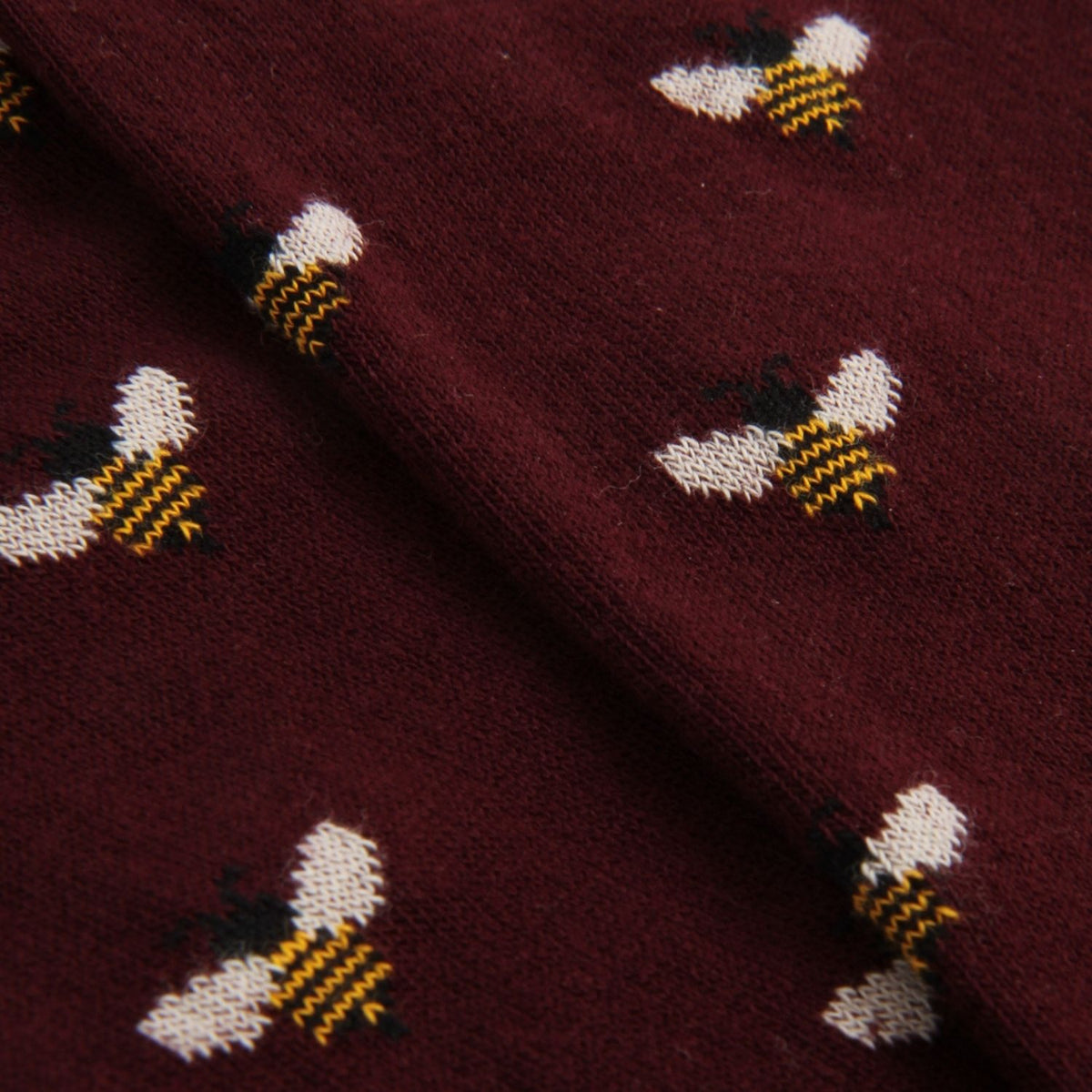 A close-up of a burgundy knit fabric featuring a repeating pattern of embroidered bumblebees in white, yellow, and black.
