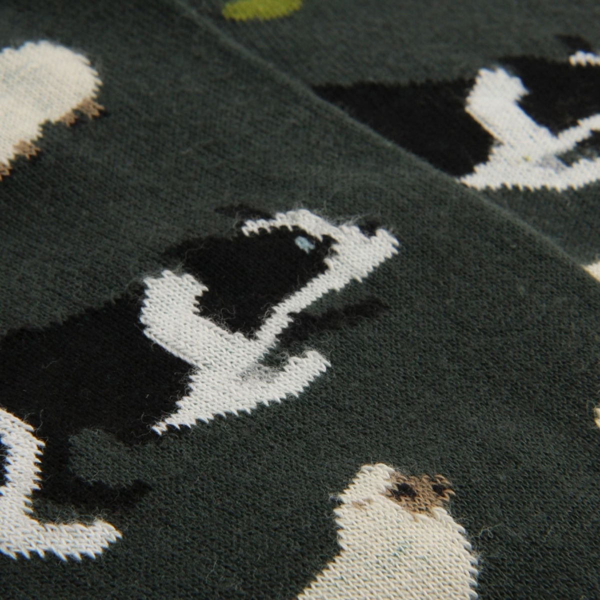 Close-up of a knit fabric with a dark green background and a repeating pattern of black-and-white dog illustrations.
