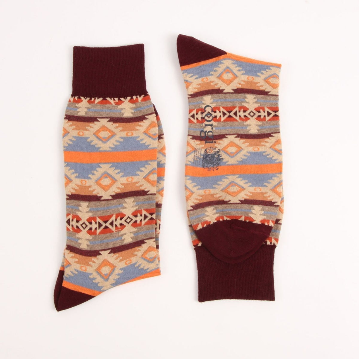 A pair of crew socks with a Southwestern geometric pattern in orange, beige, light blue, and dark brown, featuring solid dark brown ribbed cuffs, heels, and toes.