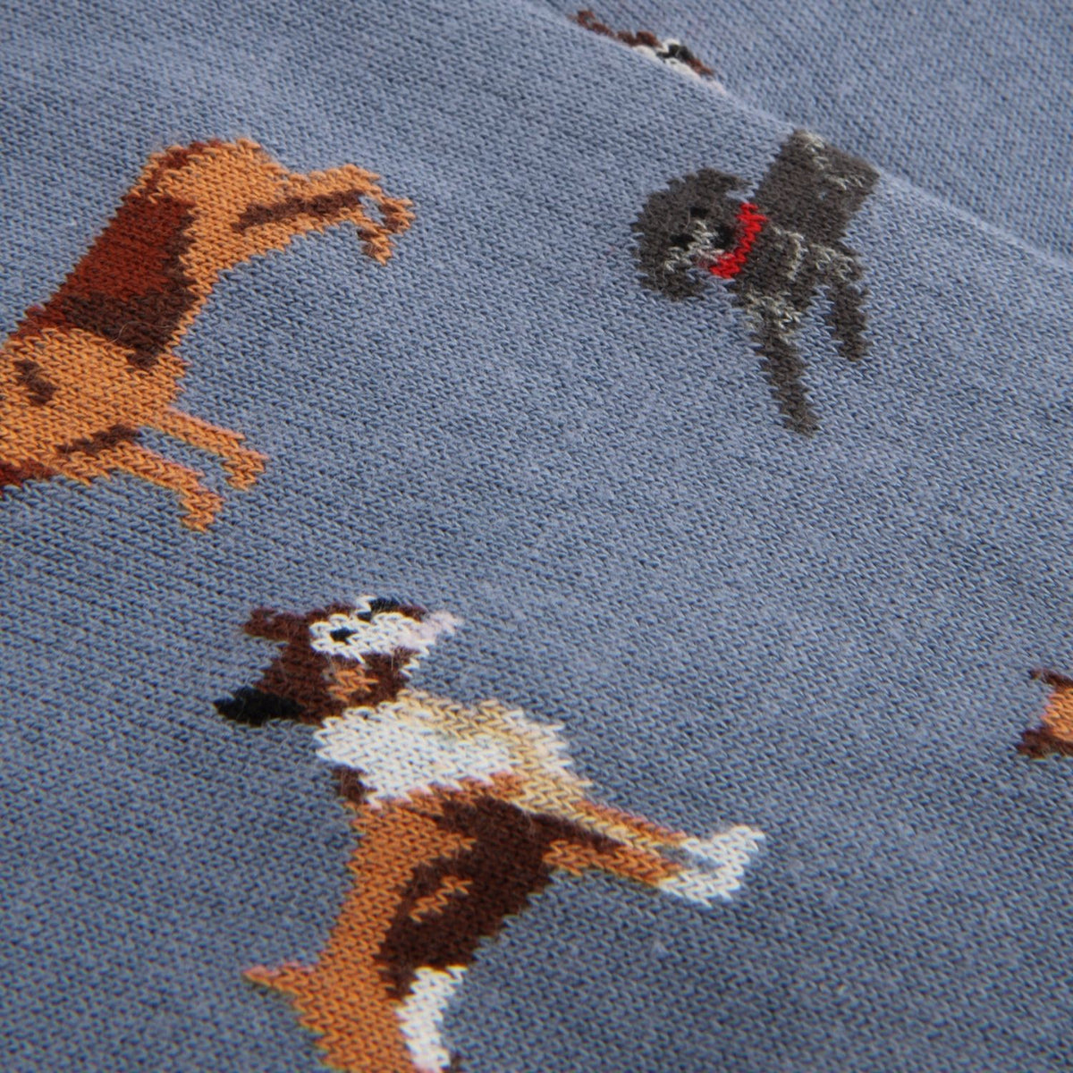Close-up of a blue knit fabric with a pattern of playful dogs in brown, white, gray, and red.