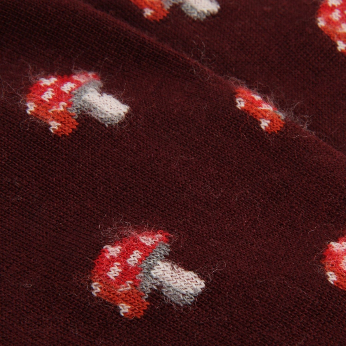 Close-up of a dark burgundy knit fabric with a repeating pattern of red and white mushrooms with gray stems.