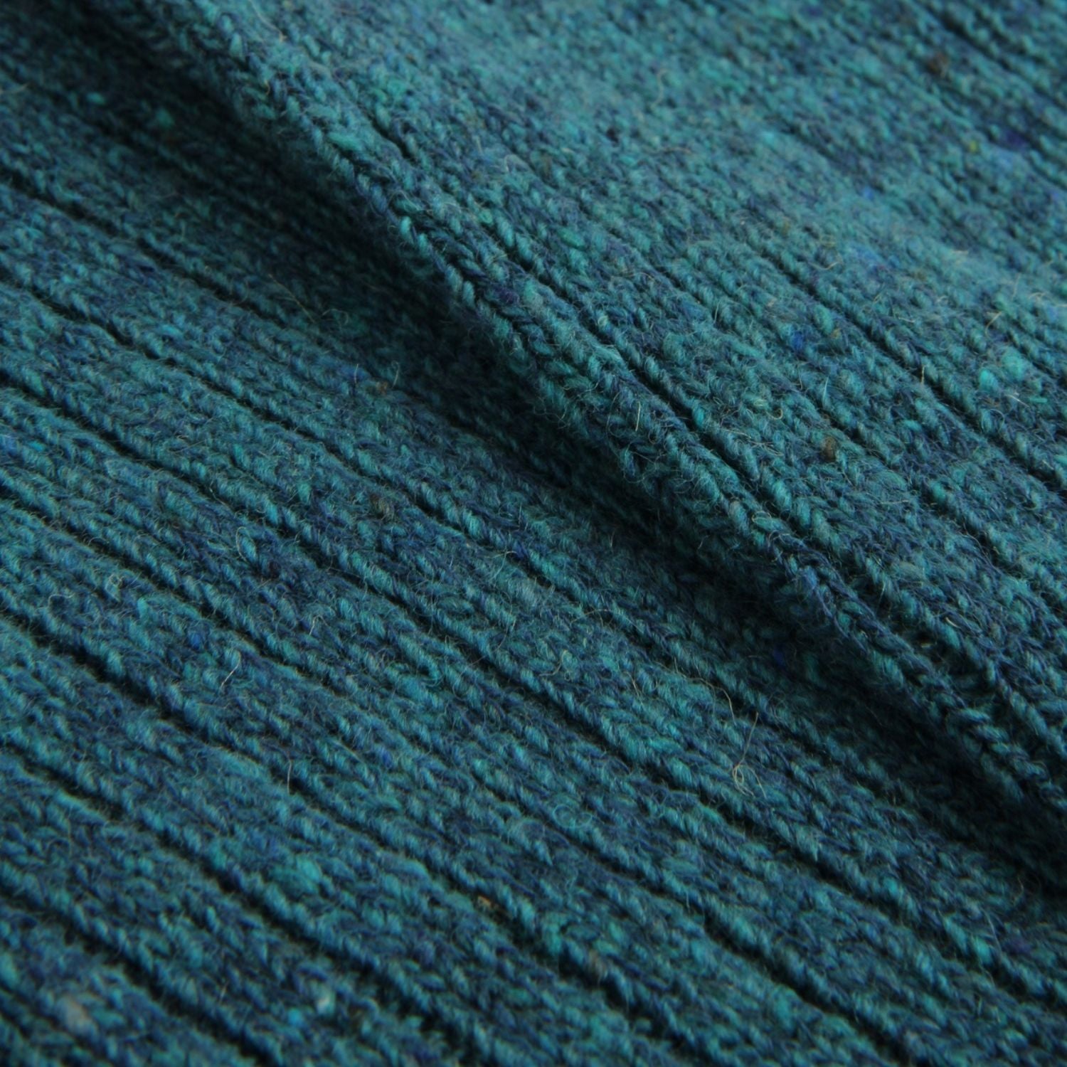 A close-up of a dark teal blue ribbed knit fabric, showing the detailed texture of the yarn and the diagonal folds.