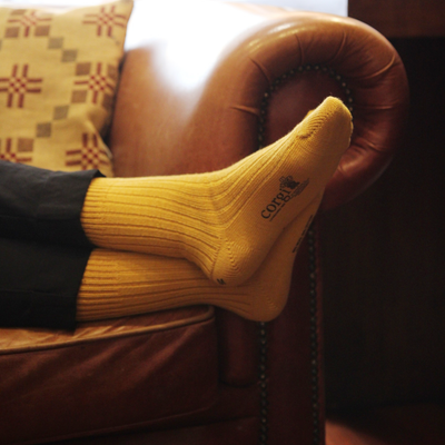 Person wearing yellow socks with a brand logo, sitting on a brown leather chair.