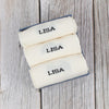 Three folded personalized socks with the name 'LISA' knitted on the side, displayed on a wooden surface.