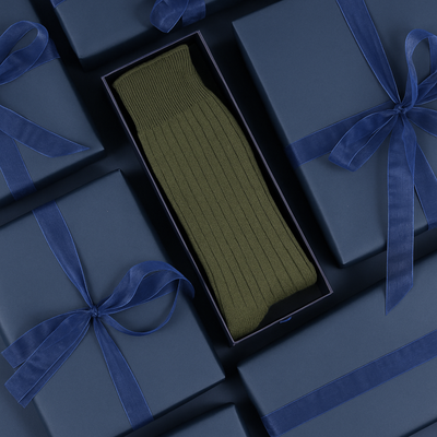 Loden green cashmere socks in a navy box with blue ribbons on a dark background
