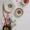 Three ceramic bowls with dried herbs and flowers on a textured surface