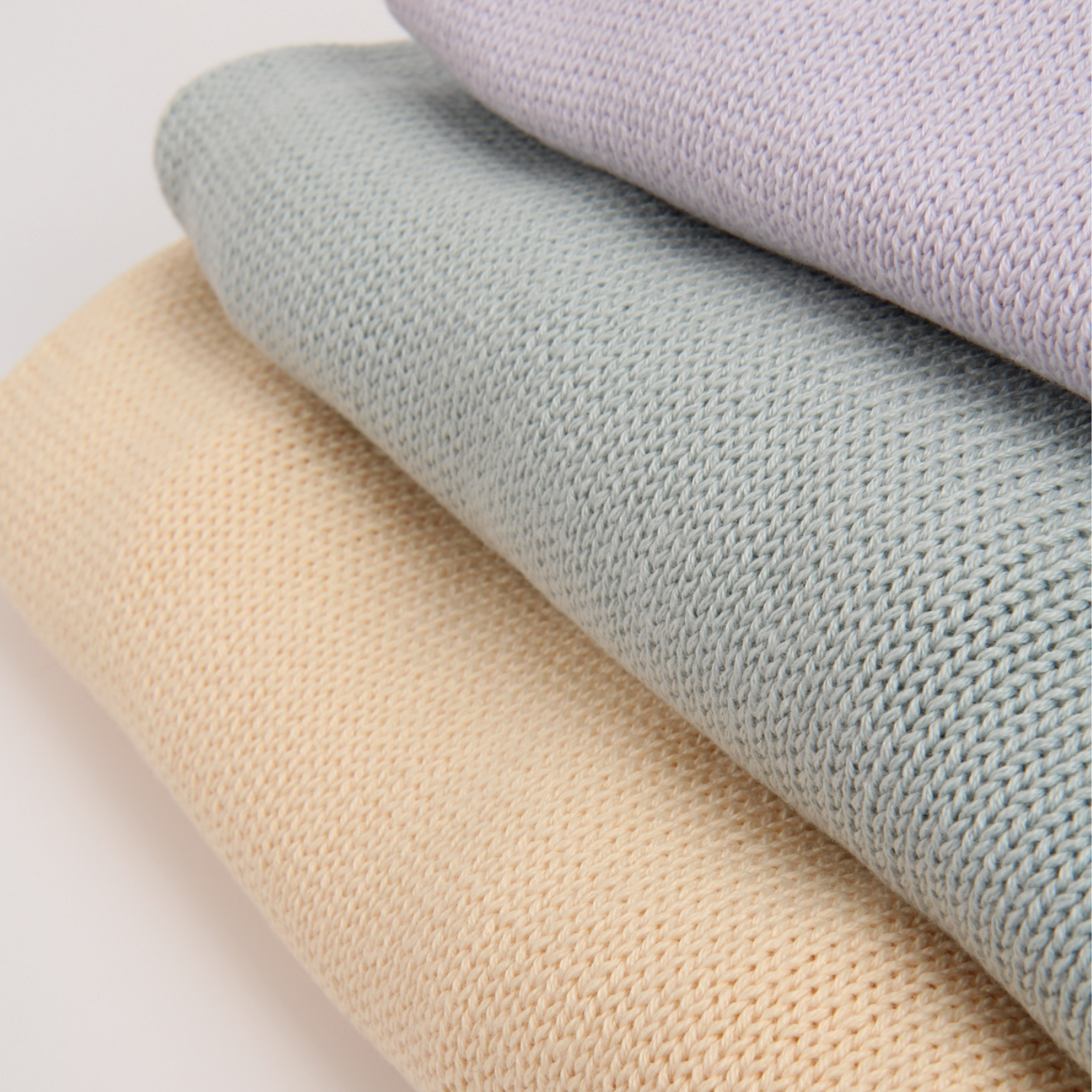 Three rolls of fabric in pale yellow, light green, and purple on a light gray background