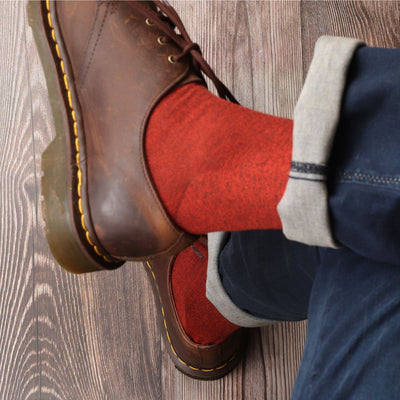 Brown leather boots with yellow stitching worn with red socks on a wooden floor.