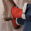 Brown leather boots with yellow stitching worn with red socks on a wooden floor.