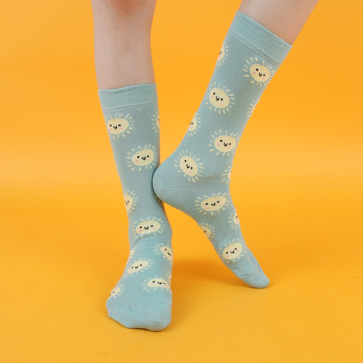 A pair of blue cotton socks with a pattern of yellow suns, displayed against a yellow background.