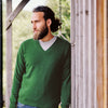A man wearing a green classic V-neck sweater with a ribbed pattern at the cuffs and hem.